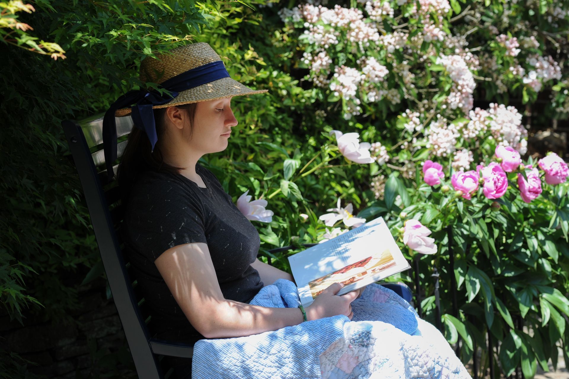 a woman in a straw hat is sitting on a bench reading a book .