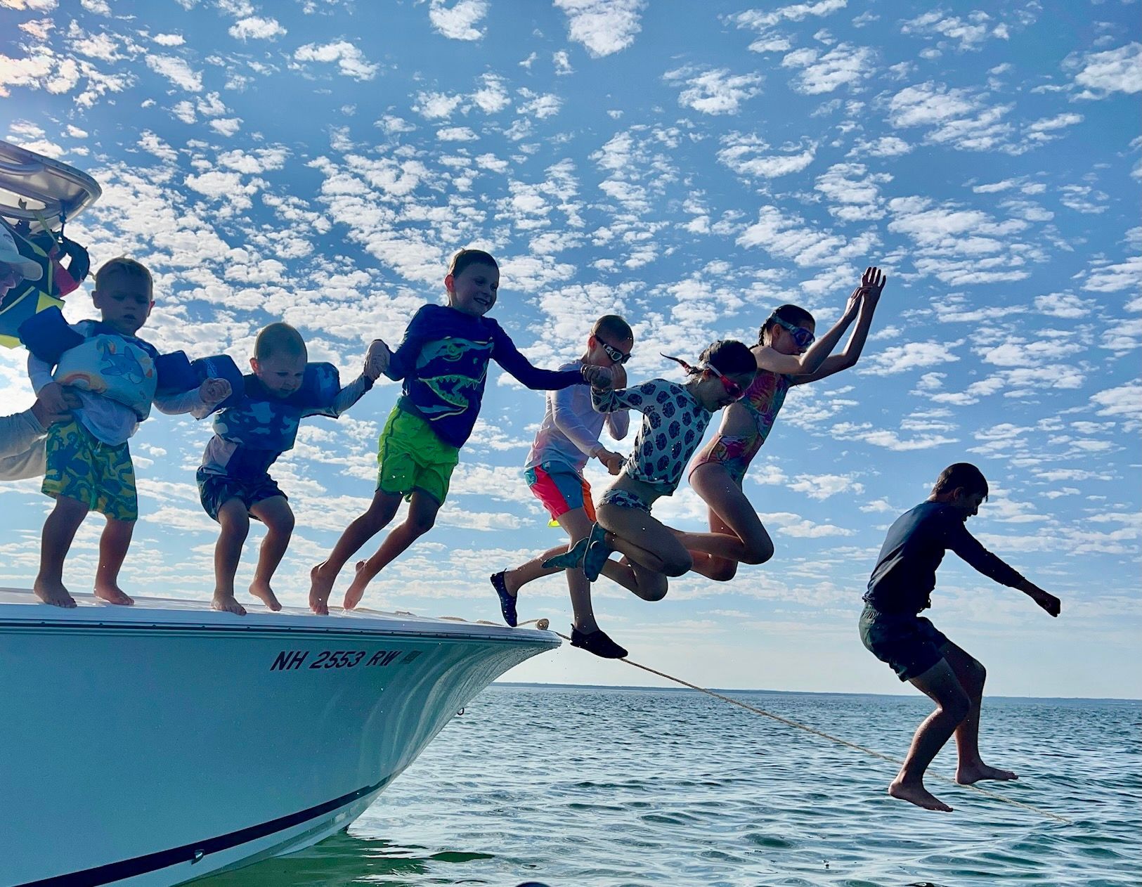 a group of children are jumping off a boat into the ocean .