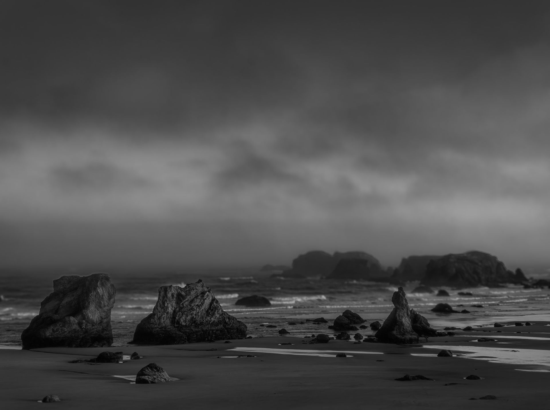 A black and white photo of a beach with rocks and a cloudy sky.