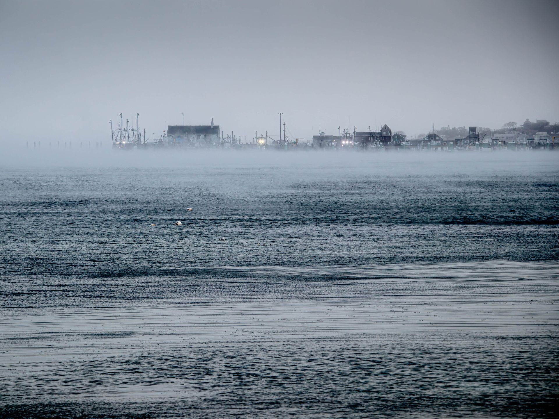 a foggy day over a body of water with a city in the background .