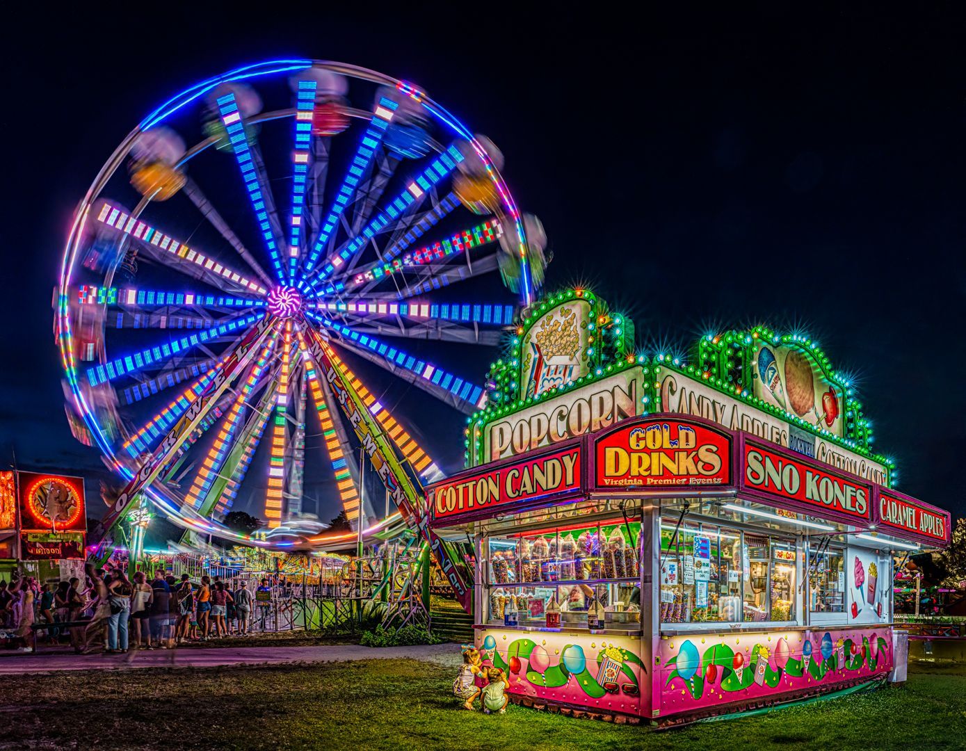 A carnival with a ferris wheel and a popcorn stand at night.