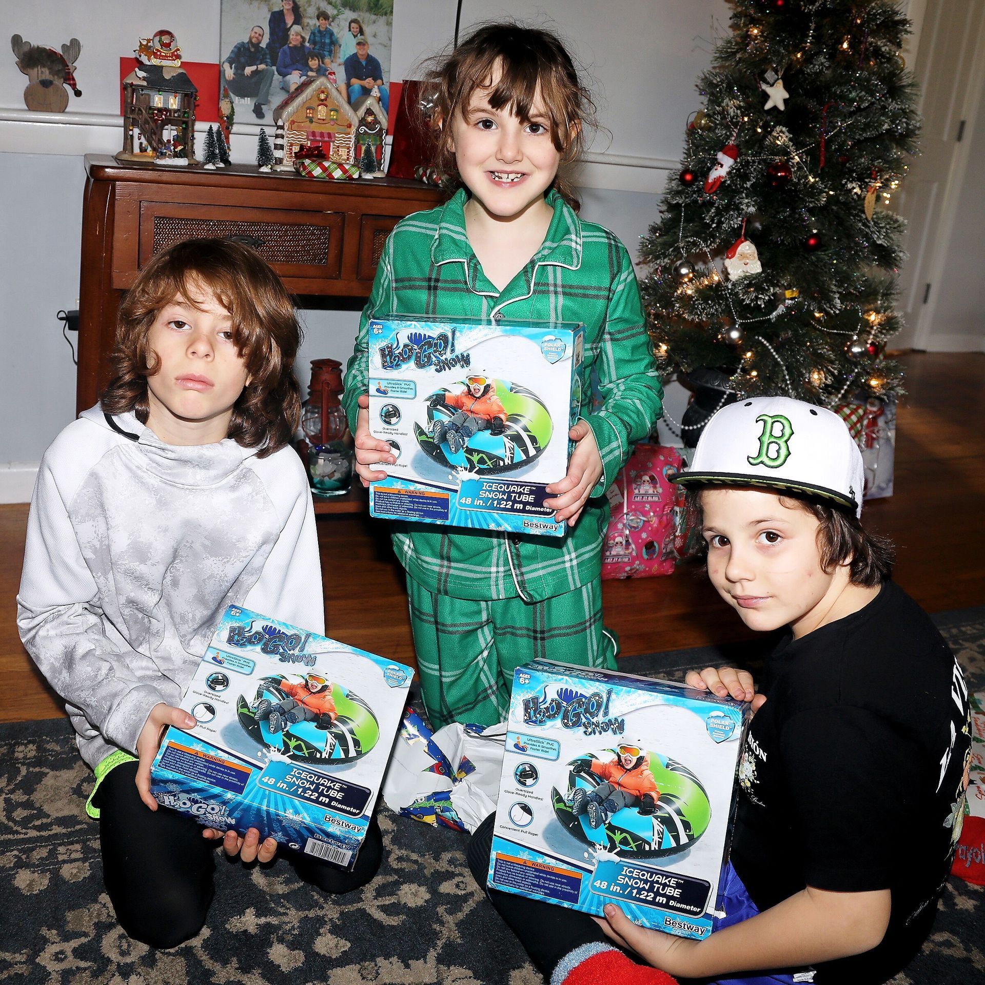 three children are holding boxes of toys in front of a christmas tree