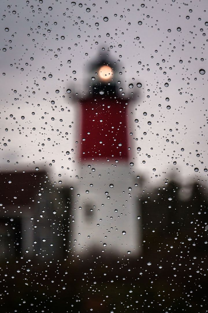 A lighthouse is visible through a window with rain drops on it