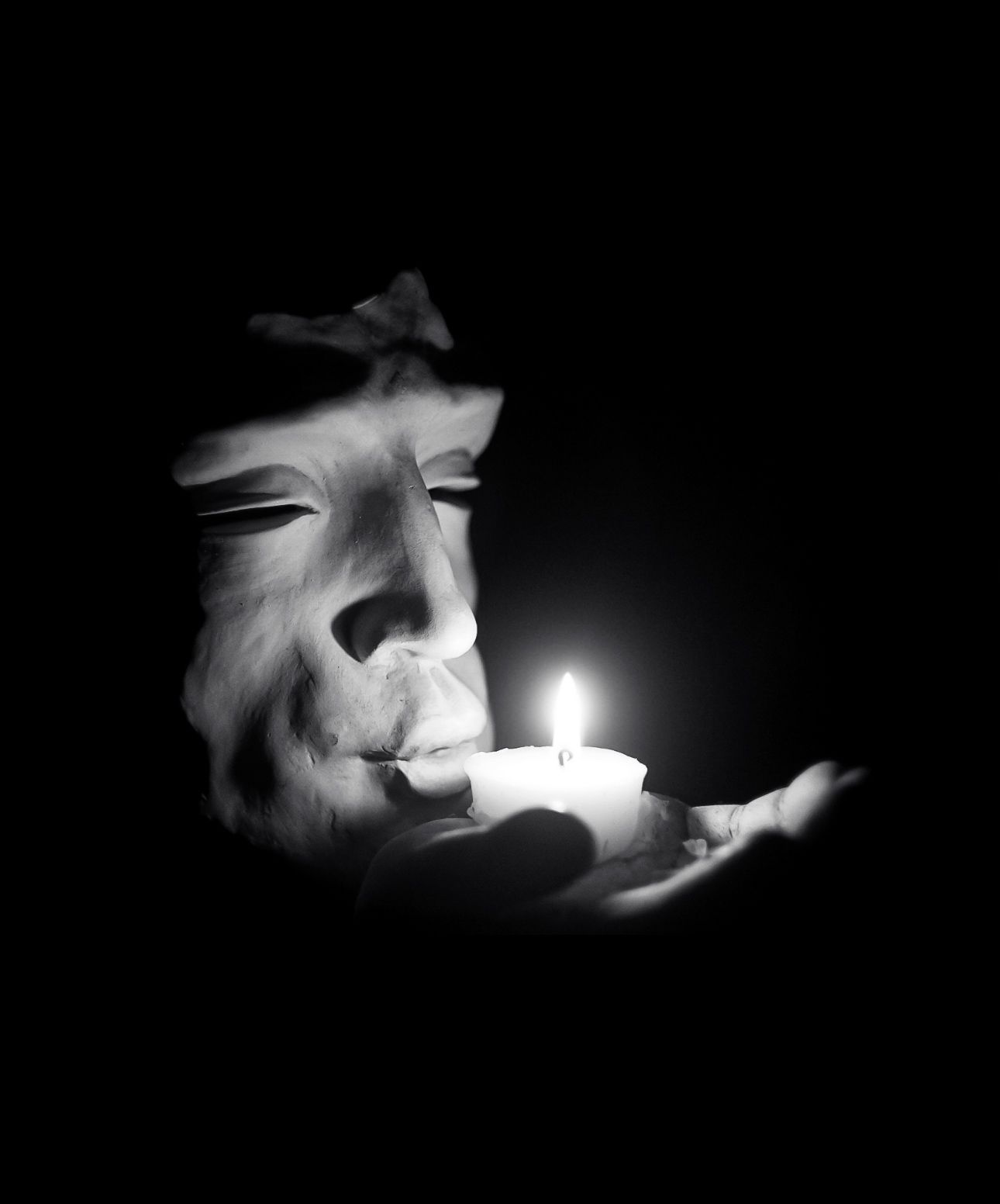 A black and white photo of a person holding a lit candle in their hand.