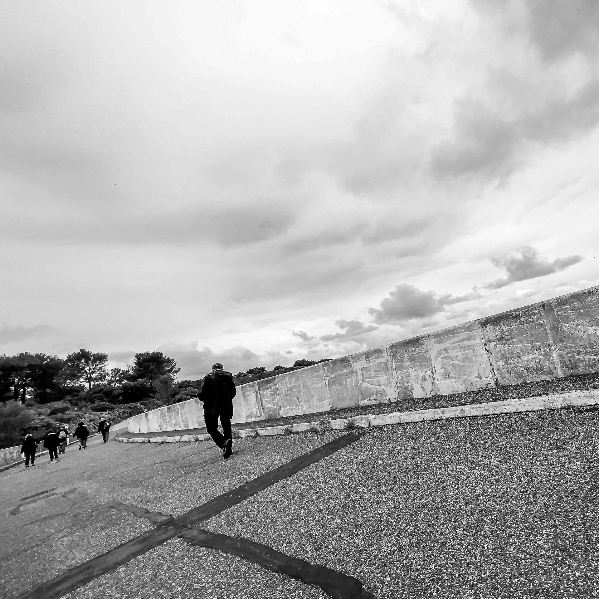 A black and white photo of a man walking down a gravel road.