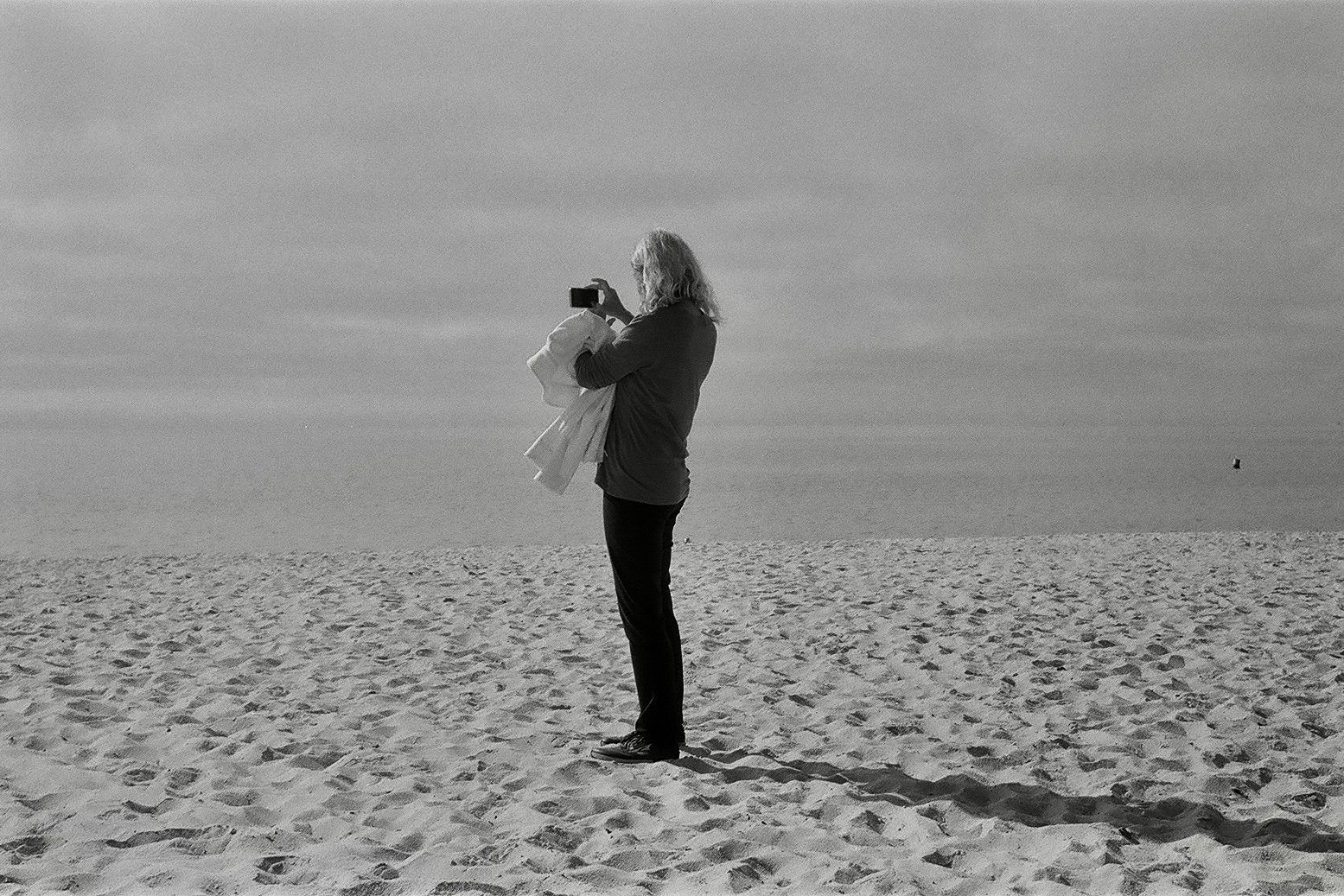A woman is standing on a beach taking a picture with a camera