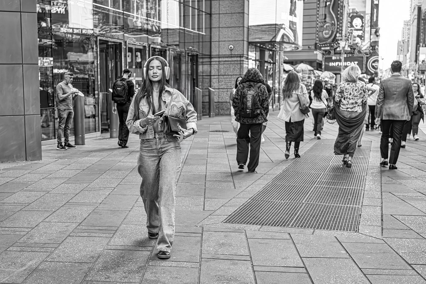 A woman wearing headphones is walking down a city street.