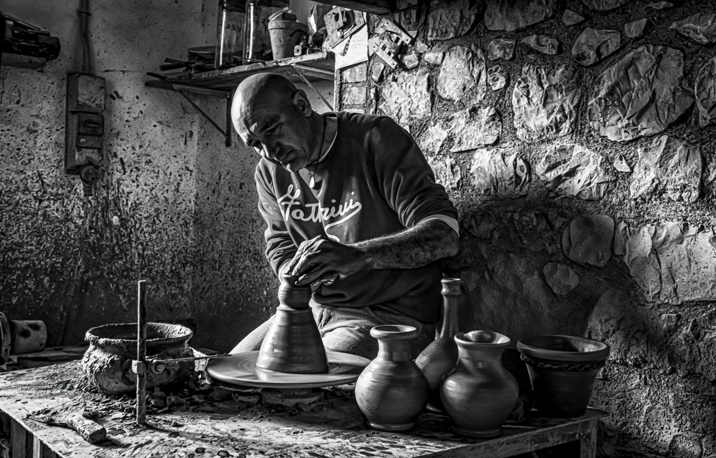 A man is making pots on a pottery wheel in a black and white photo.