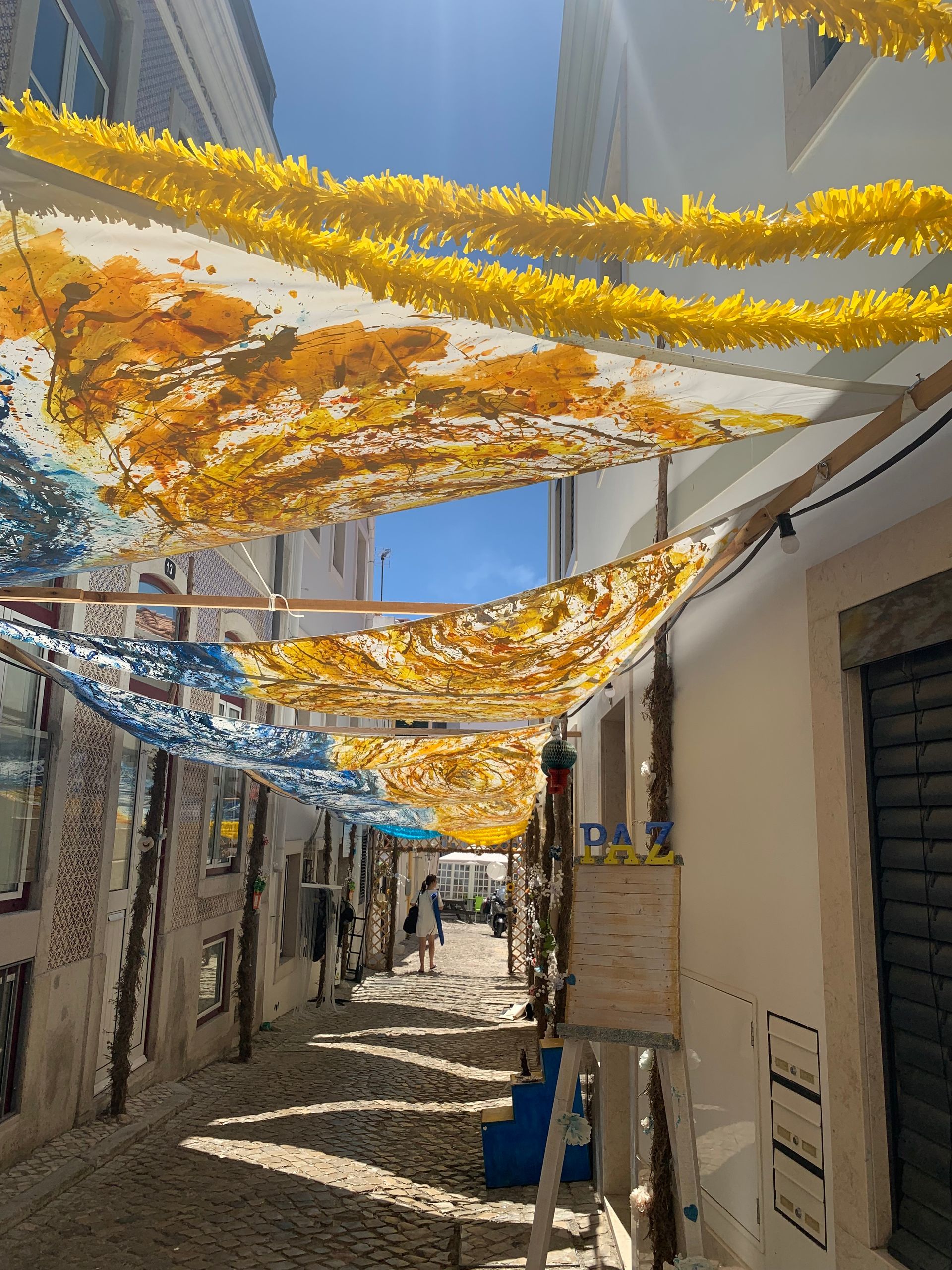 a narrow alleyway with yellow and blue decorations hanging from the ceiling