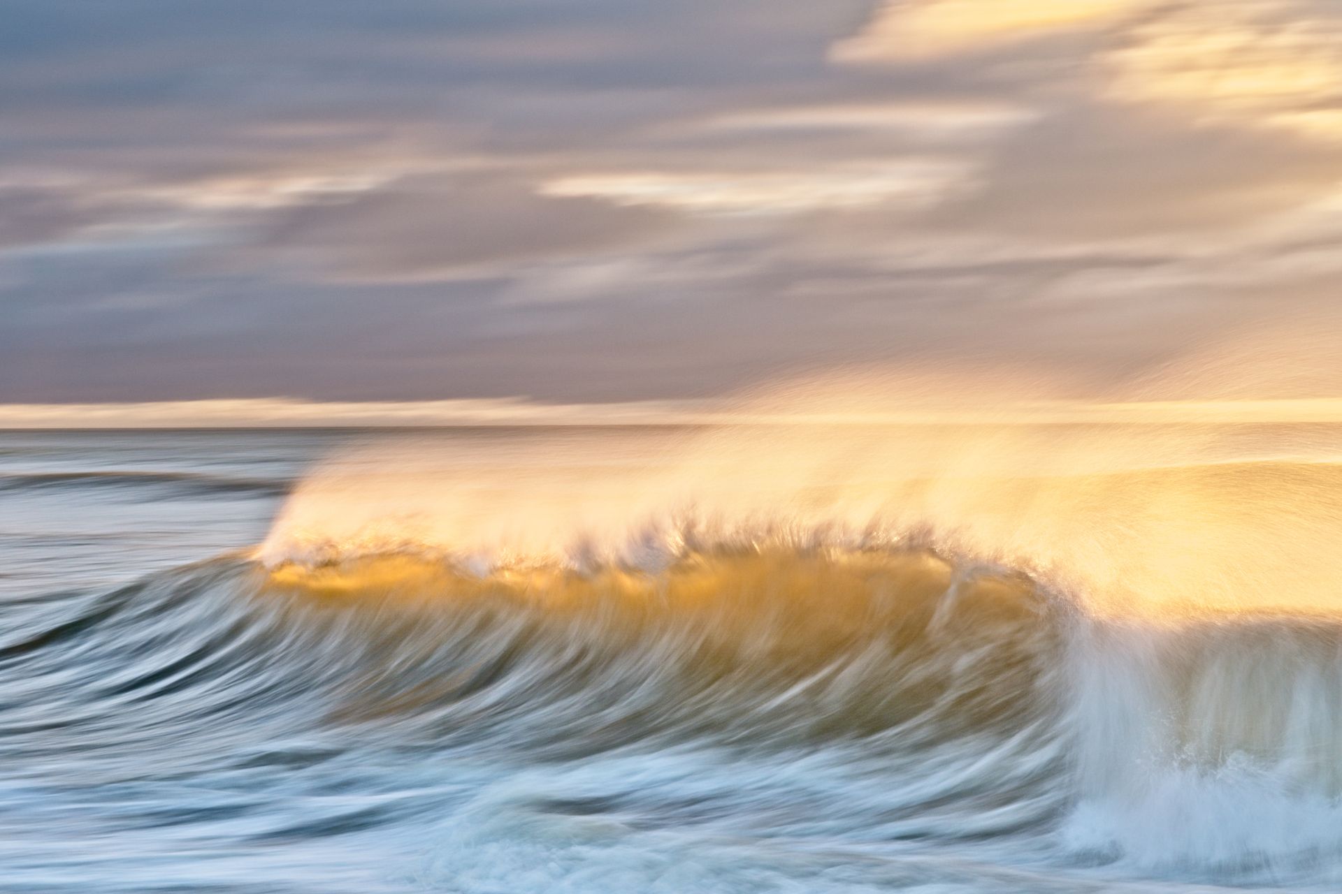 a wave is breaking in the ocean at sunset .