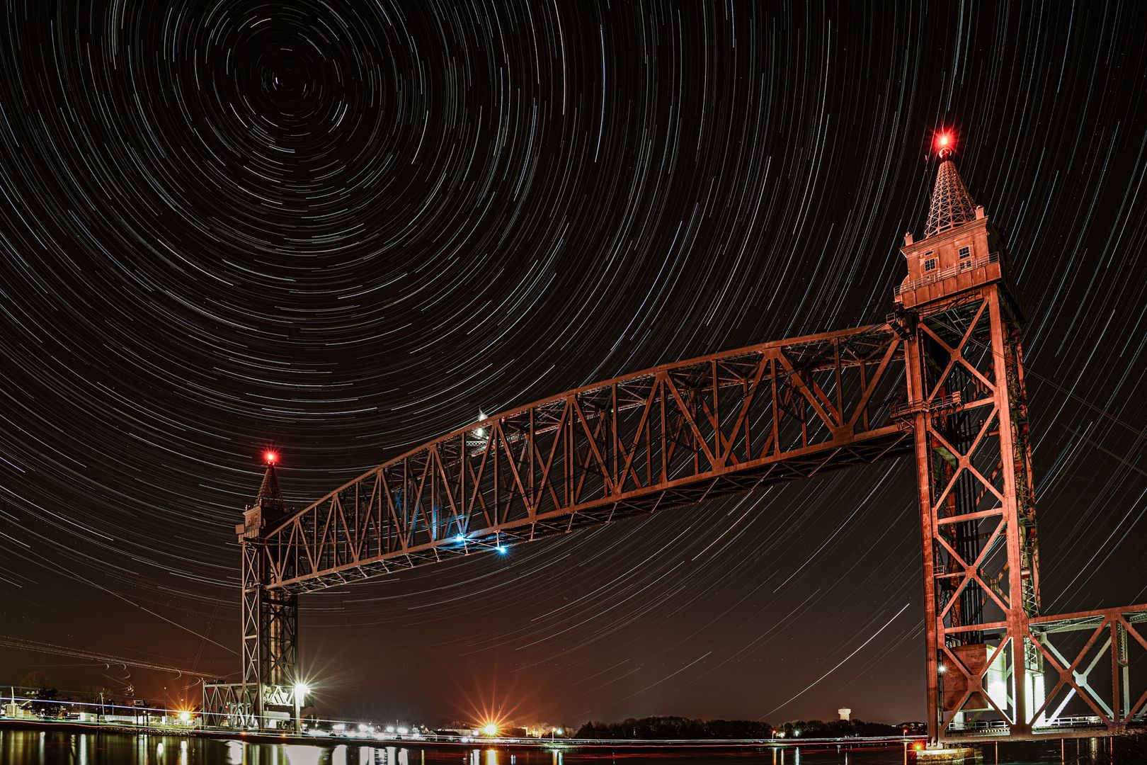A bridge over a body of water at night with a lot of stars in the sky.