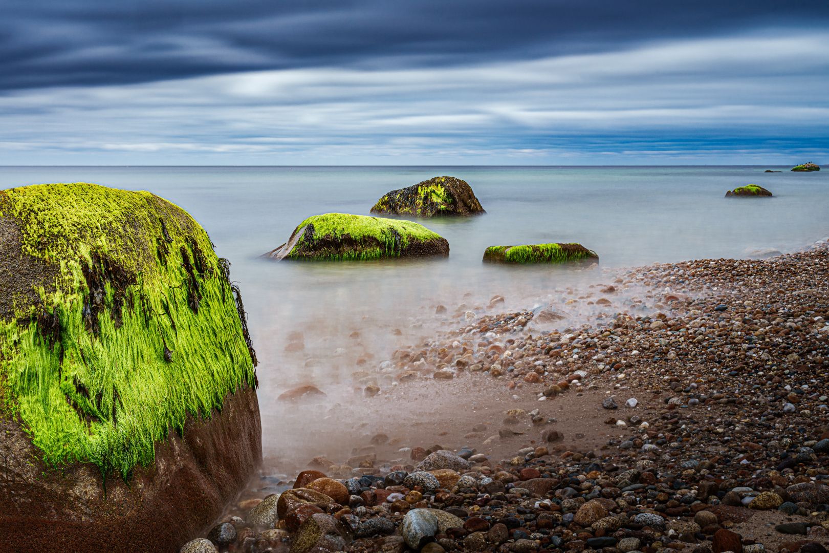 A rock covered in green algae on a beach next to the ocean.
