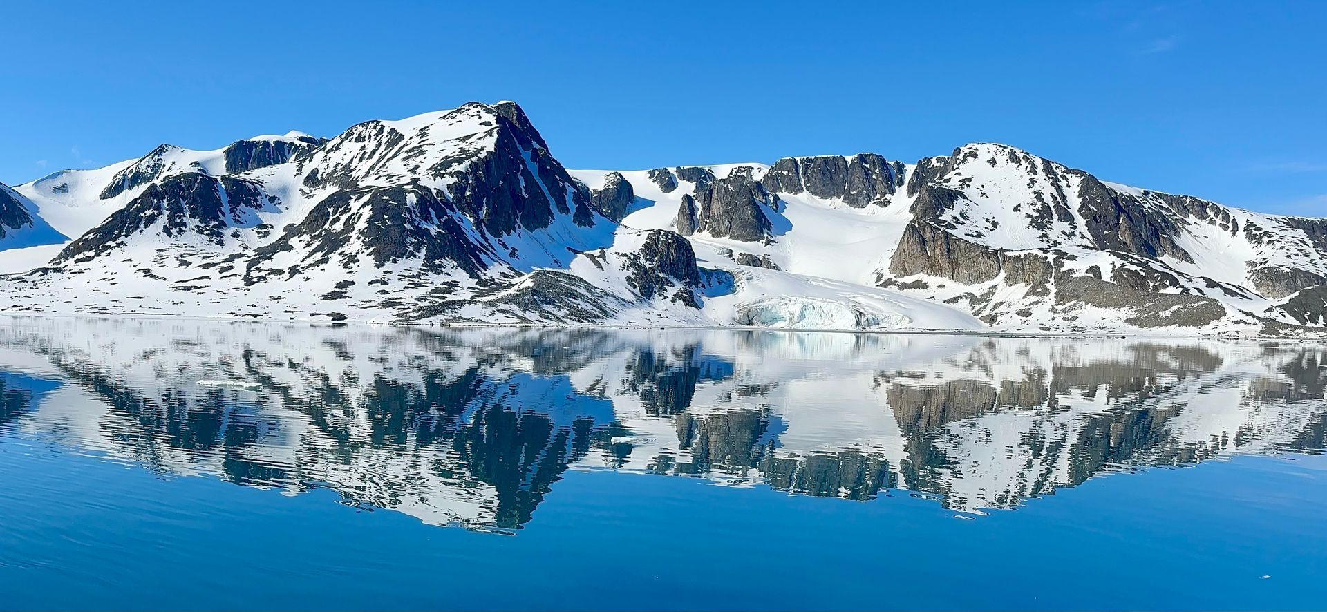 a snowy mountain is reflected in a lake .