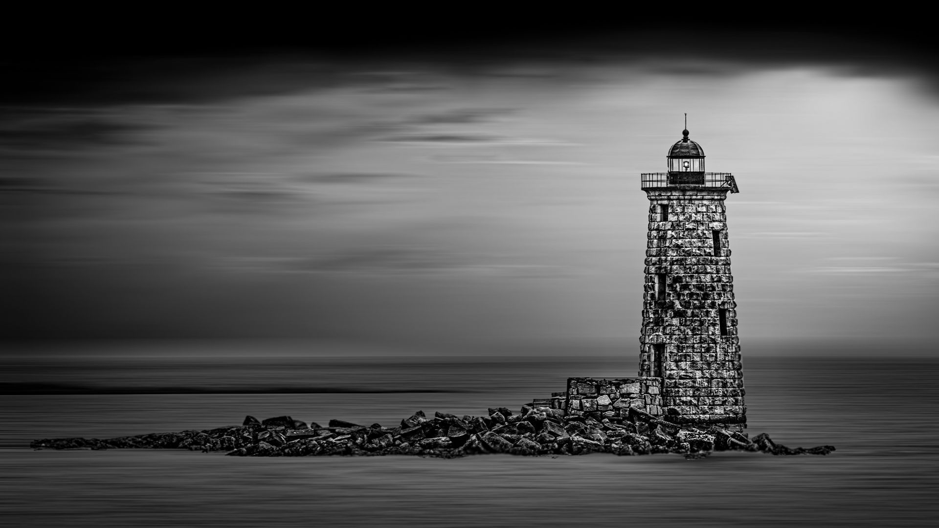 A black and white photo of a lighthouse on a small island in the middle of the ocean.