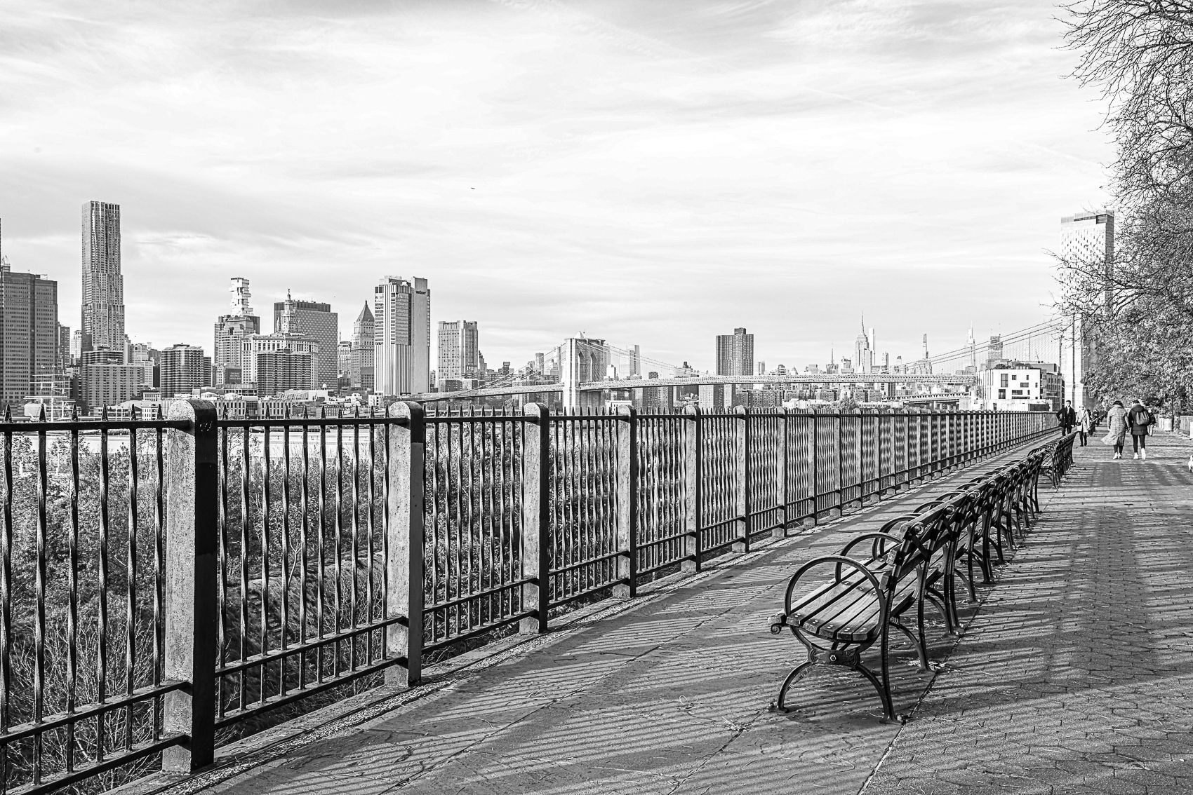 A black and white photo of a park bench with a city skyline in the background.