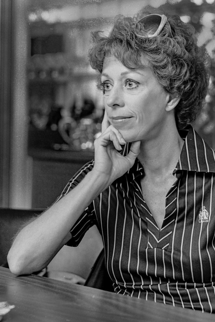 A woman in a striped shirt is sitting at a table with her hand on her chin.