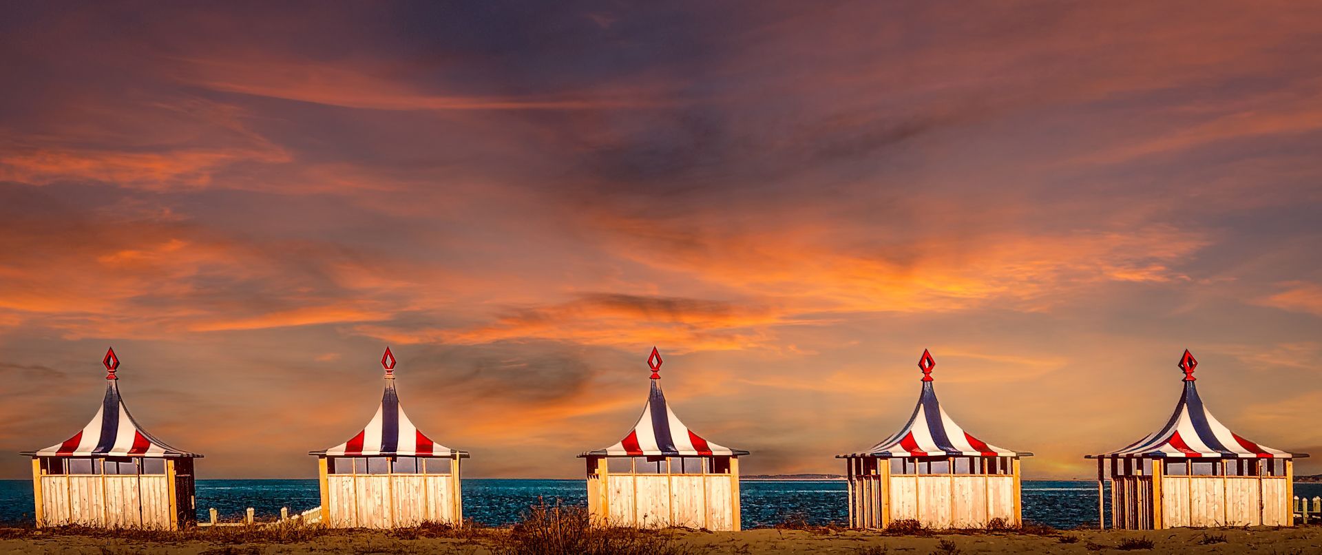 A row of circus tents on a beach at sunset.
