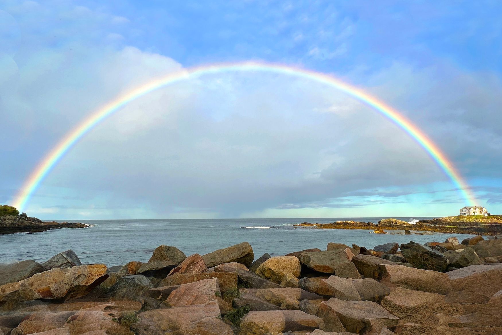 a rainbow over the ocean with rocks in the foreground