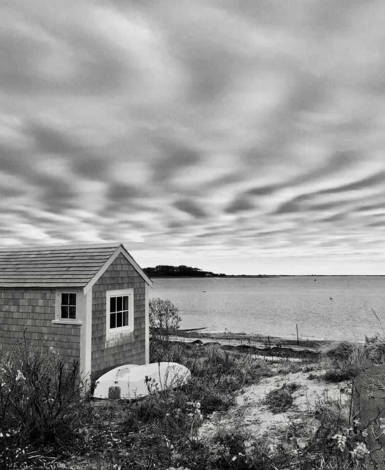 A black and white photo of a shed on the shore of a body of water