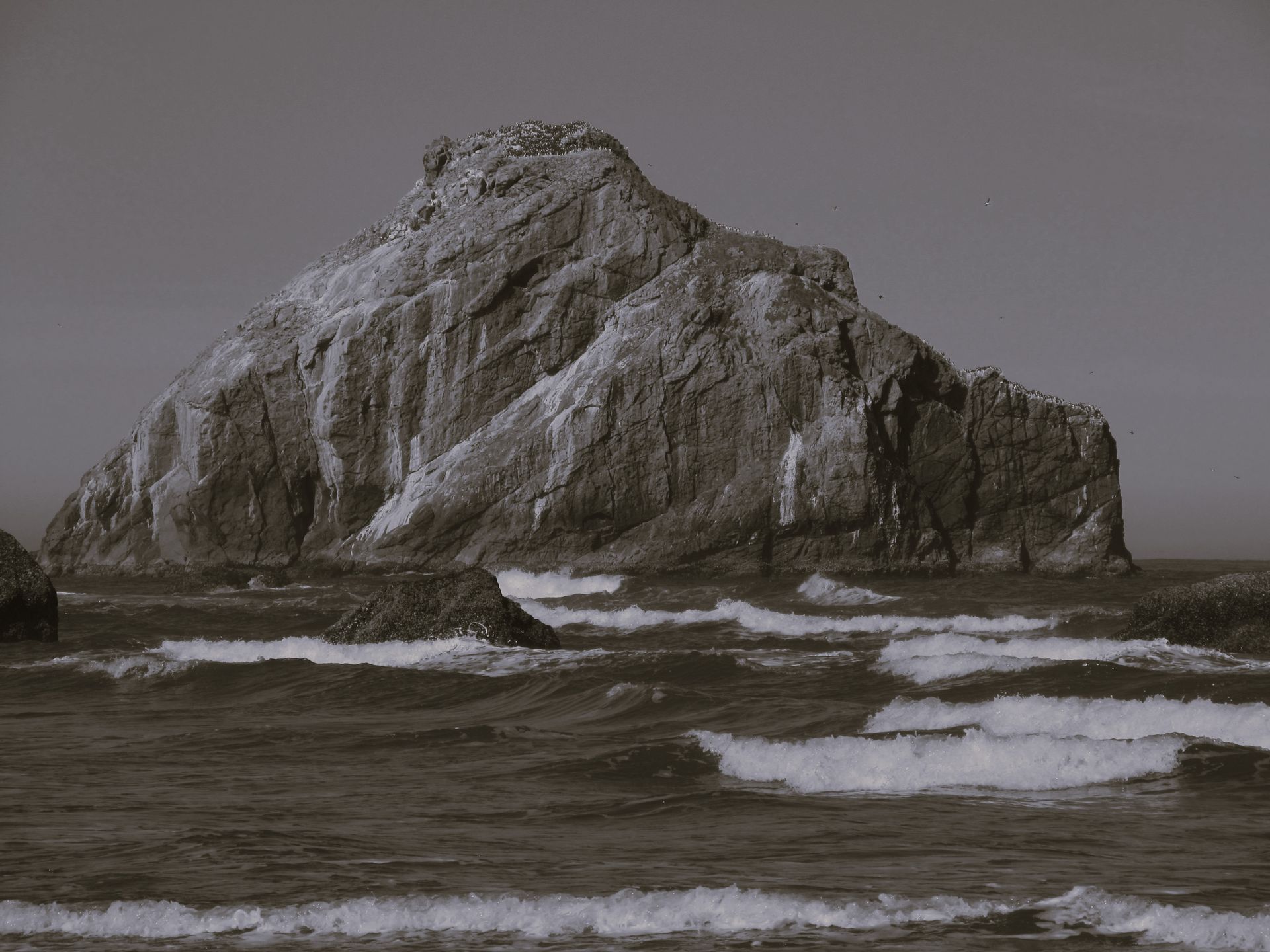 A black and white photo of a large rock in the middle of the ocean.