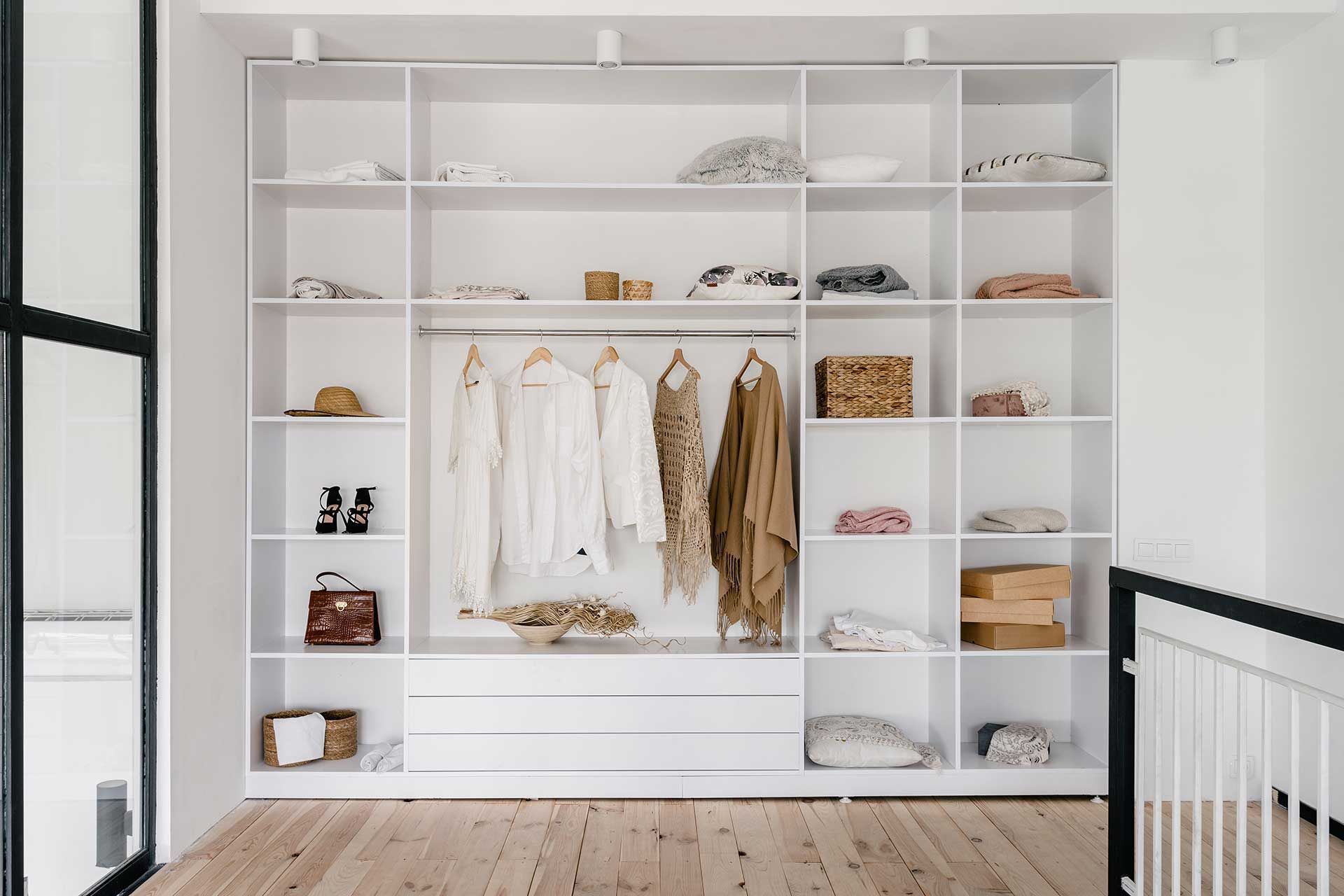 White walk-in closet with shelves, hanging clothes, and drawers on a wooden floor.