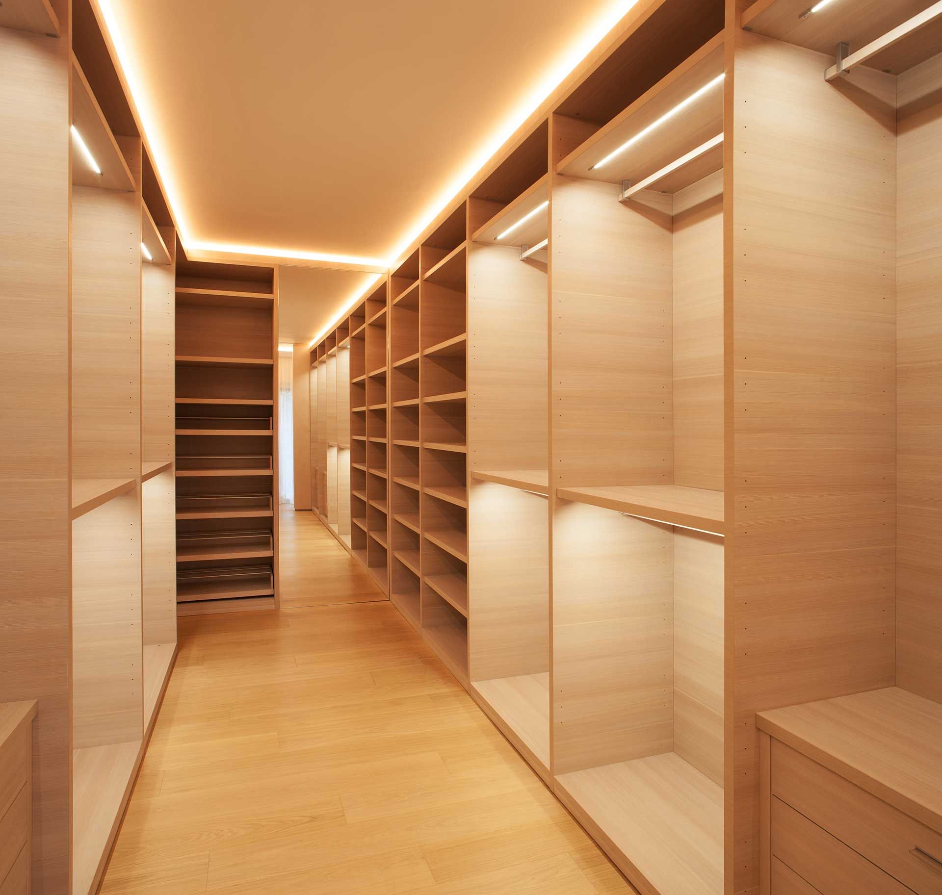 Wooden walk-in closet with shelves and drawers, lit by recessed lighting.