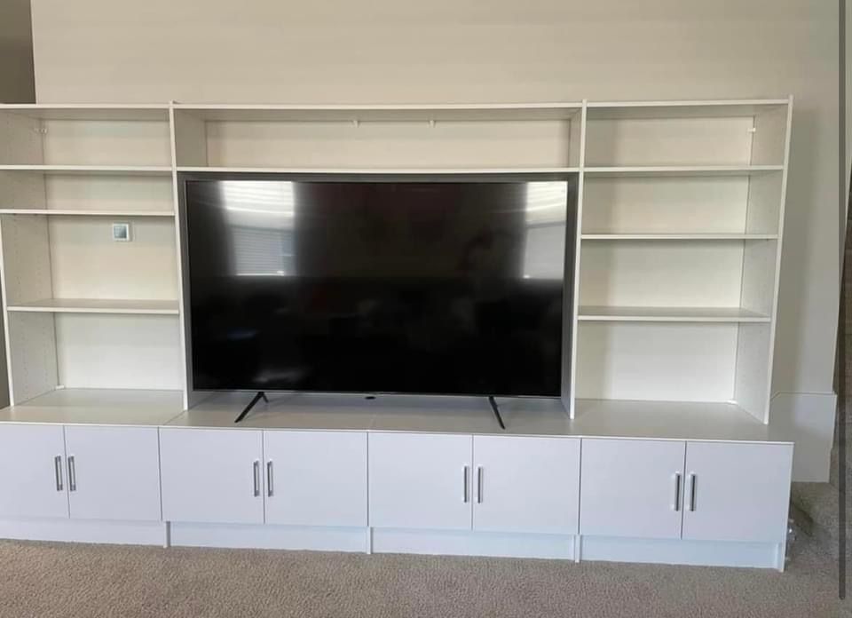 White entertainment center with built-in shelves surrounding a large black TV, on a beige carpet.