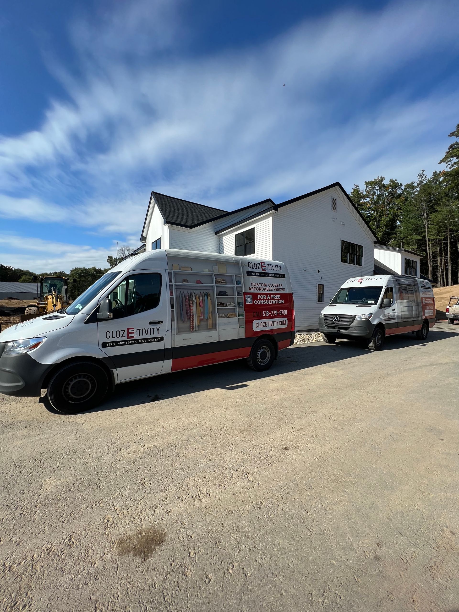 Two white service vans parked in front of a white house under construction.