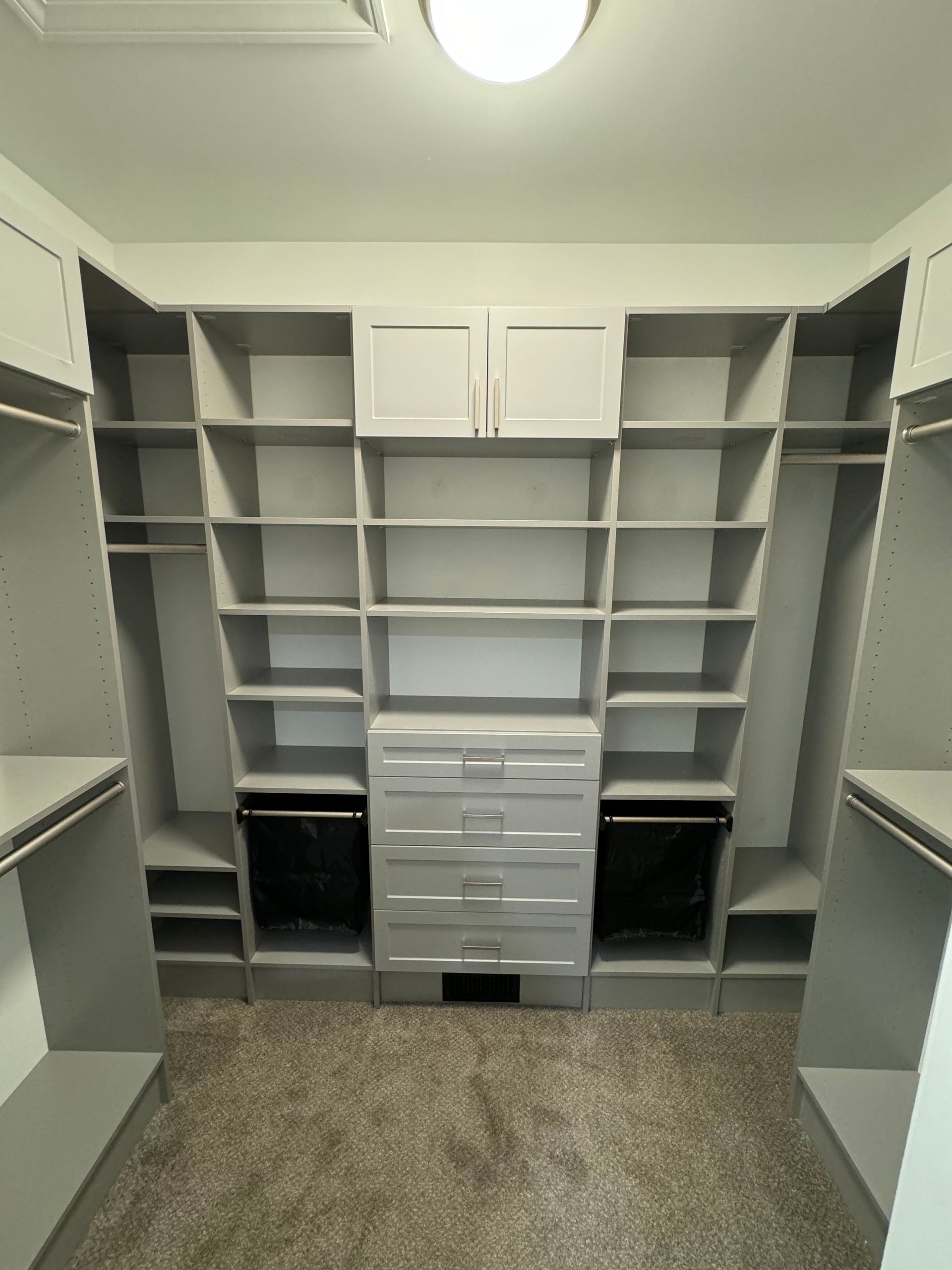 Walk-in closet with gray shelving, drawers, and hanging rods; tan carpet.