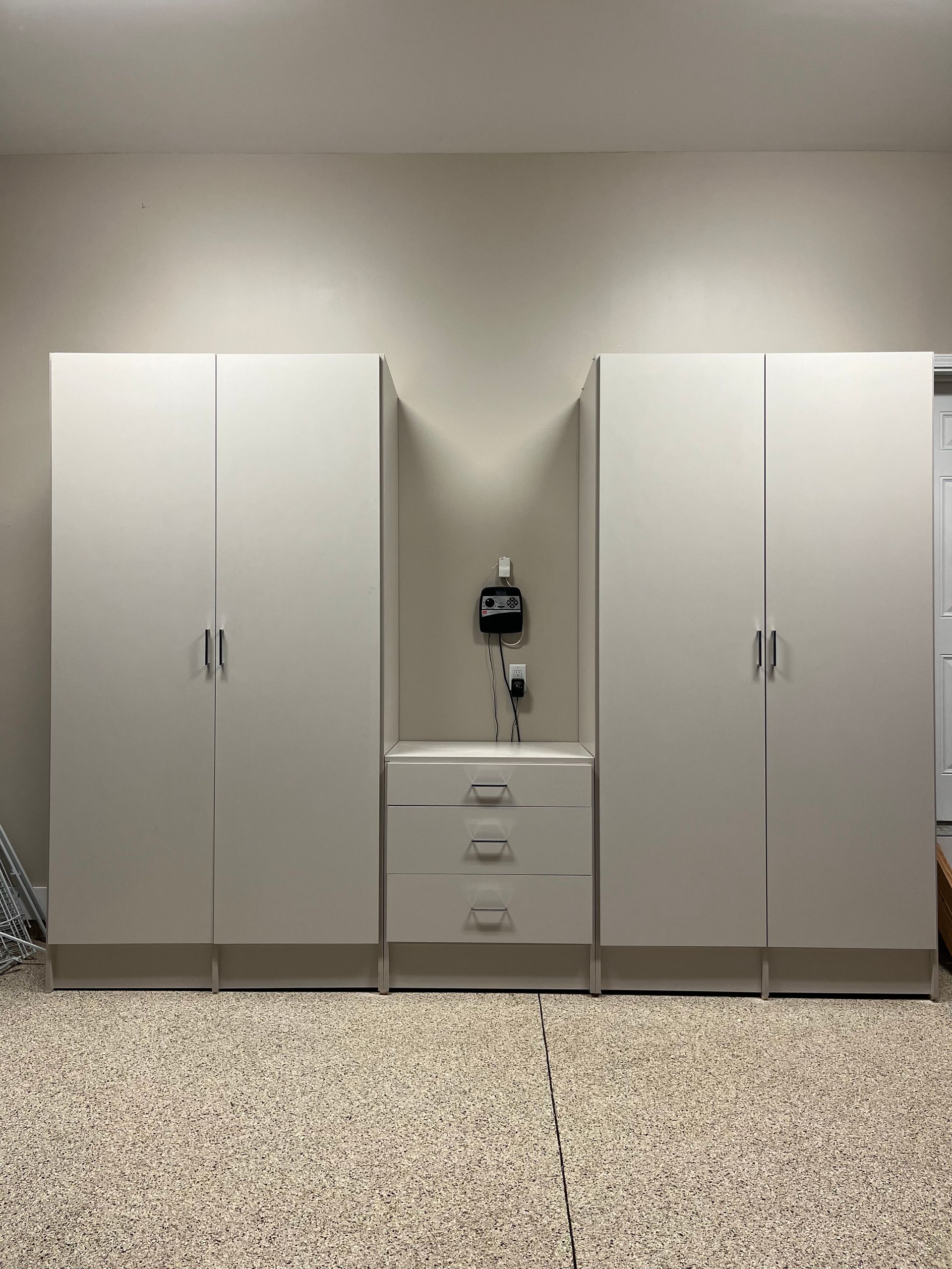 Garage storage cabinets: white tall cabinets flank a central unit with drawers and a key rack, against a light wall.