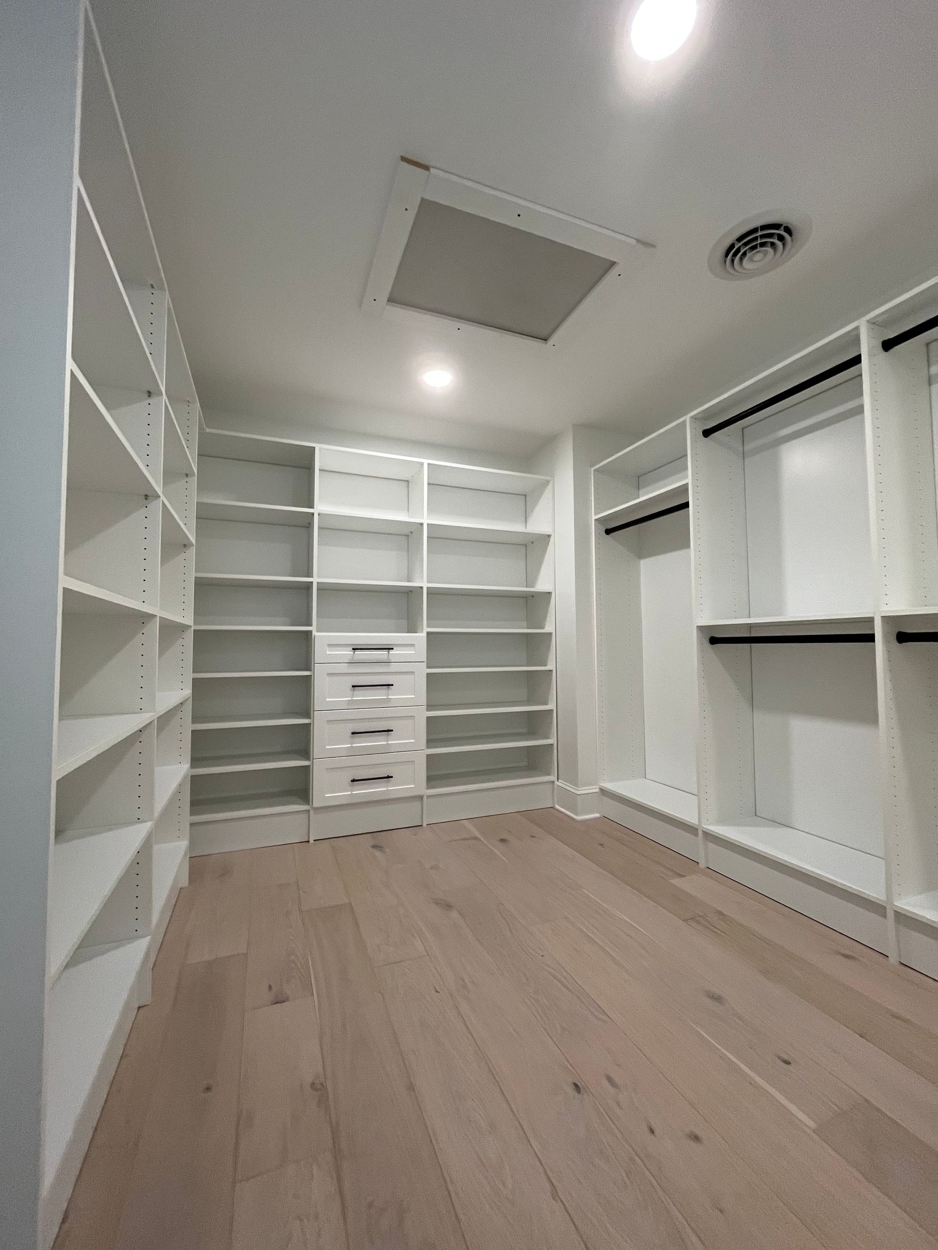 White walk-in closet with shelving and drawers, wood floor, and overhead lighting.