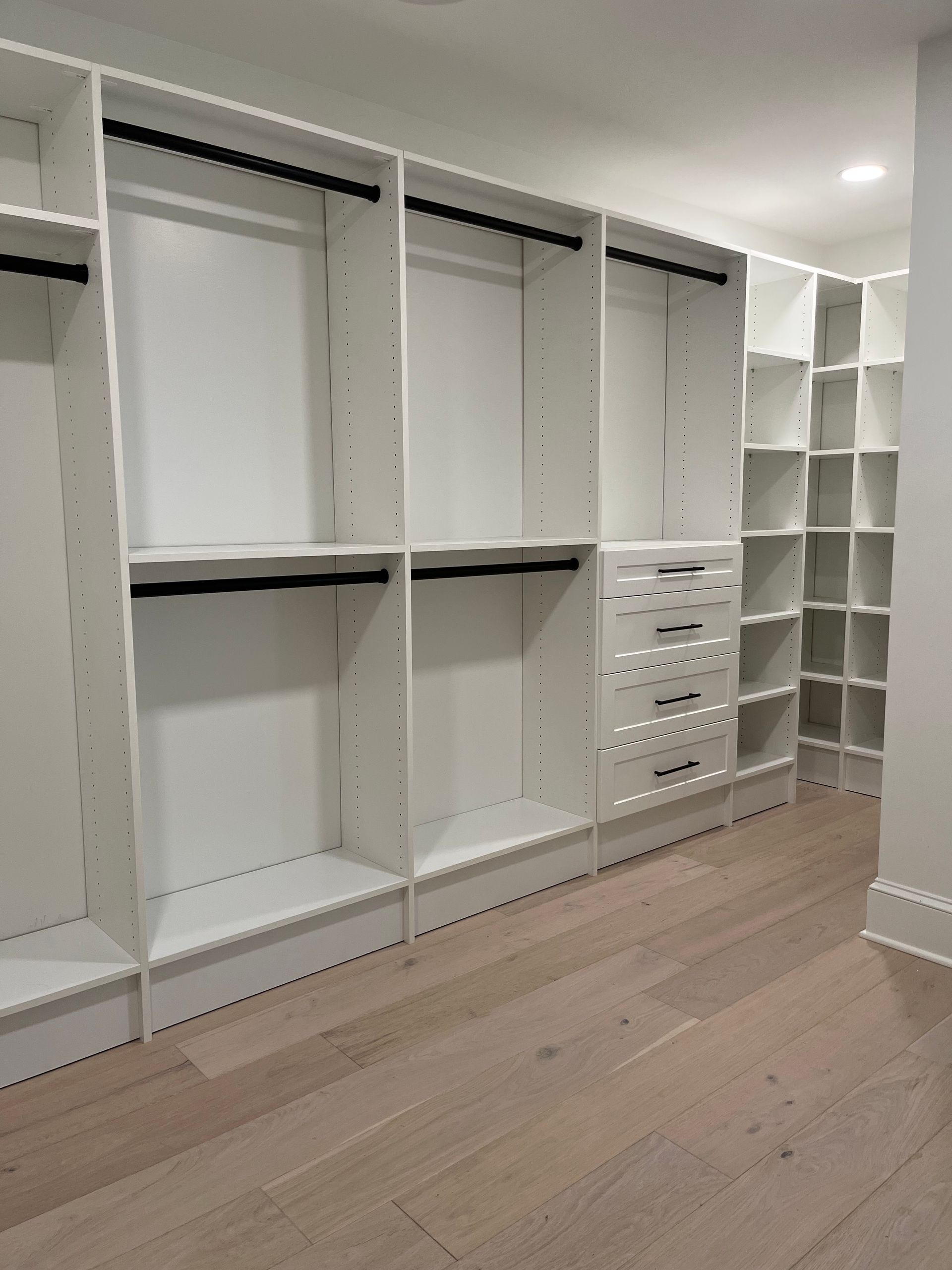 White walk-in closet with empty shelving and hanging rods, light wood floor.