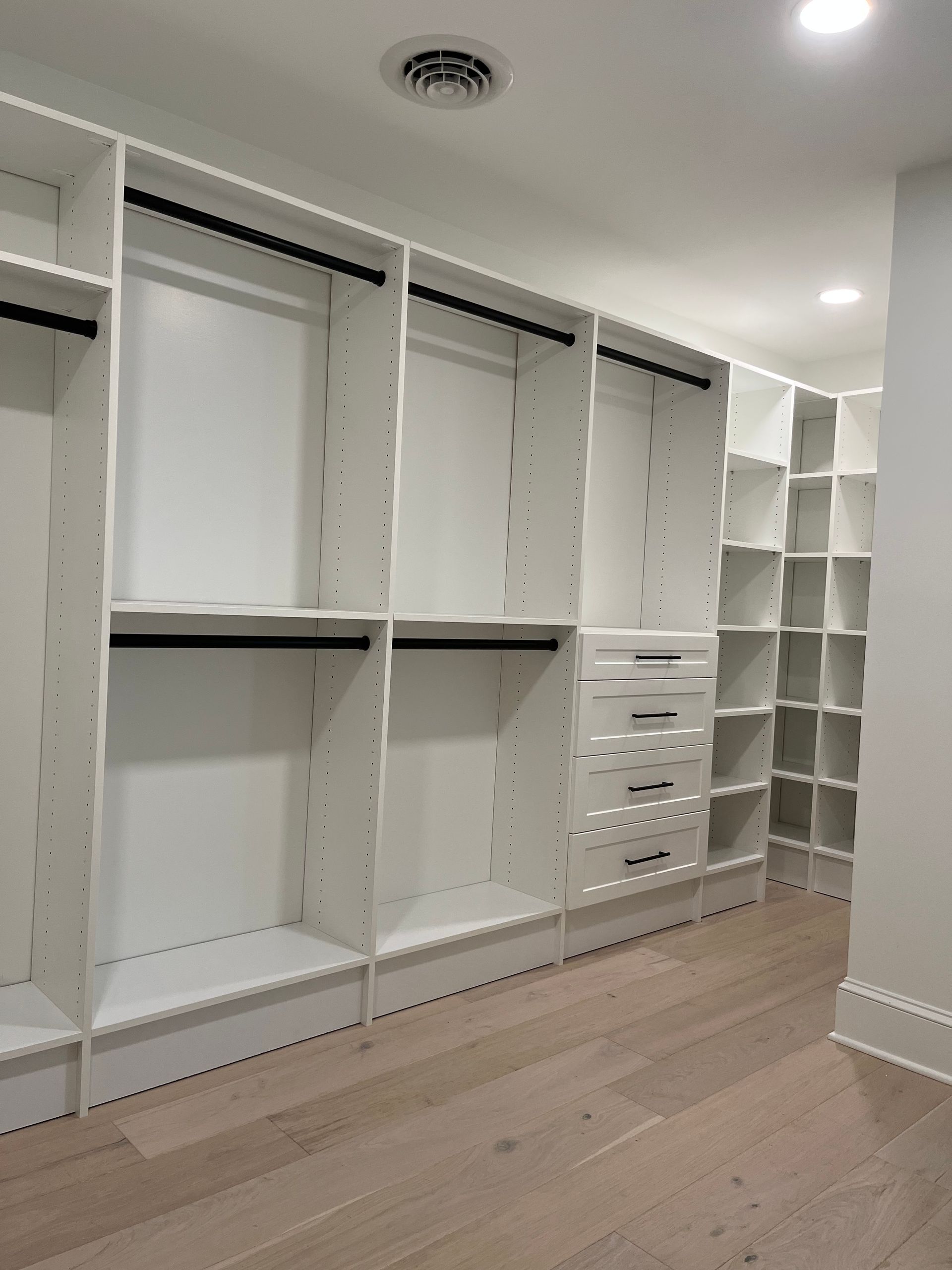 Empty white custom closet with shelves and drawers on light wood floor.