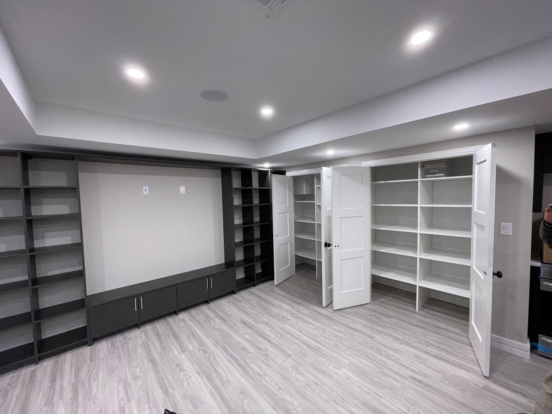 Gray built-in bookshelves and cabinets on a white wall. White storage closet with open doors and light gray flooring.