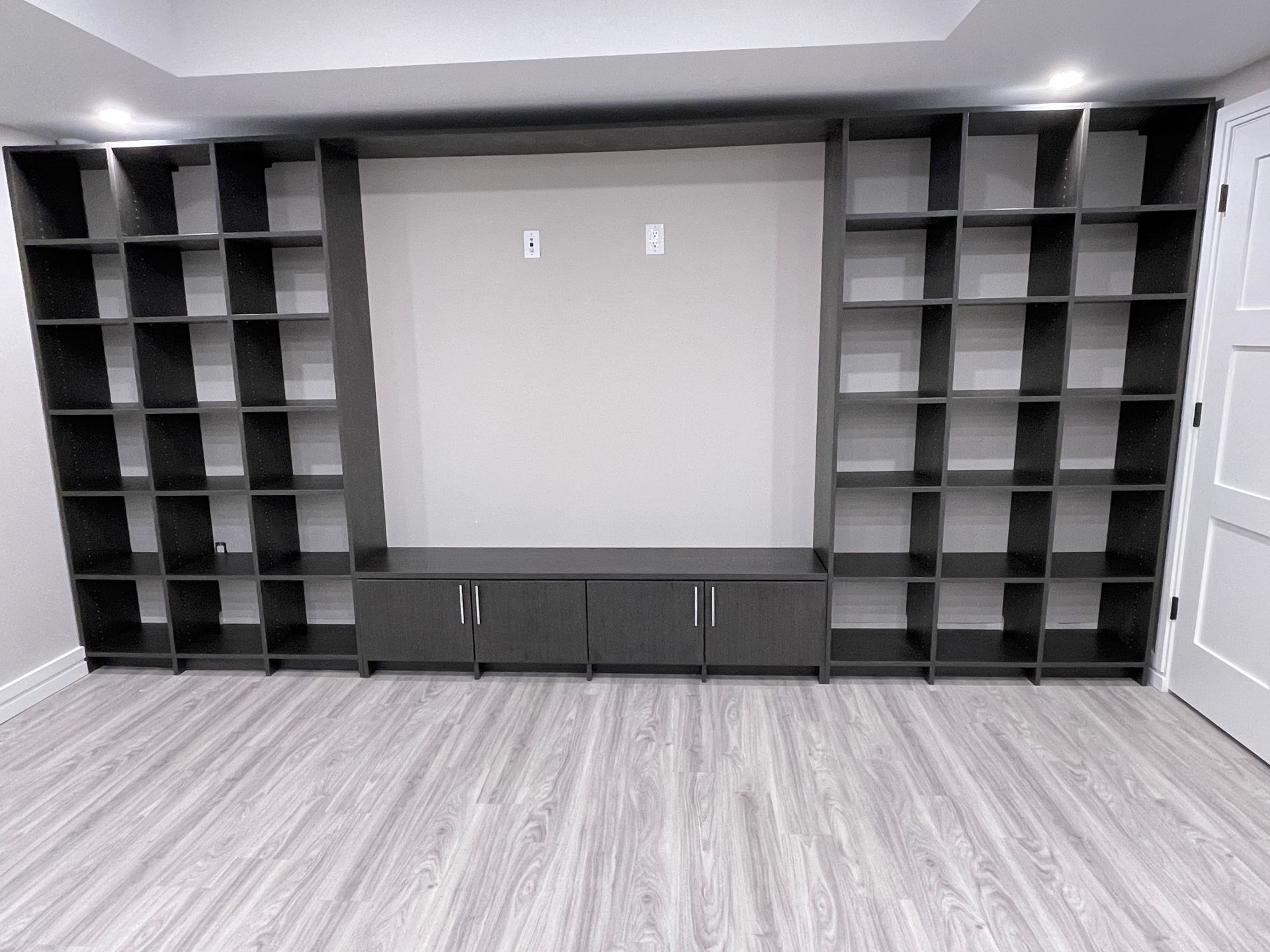 Dark gray built-in shelves flanking a gray media console with a blank wall for a TV in a room with light wood floors.