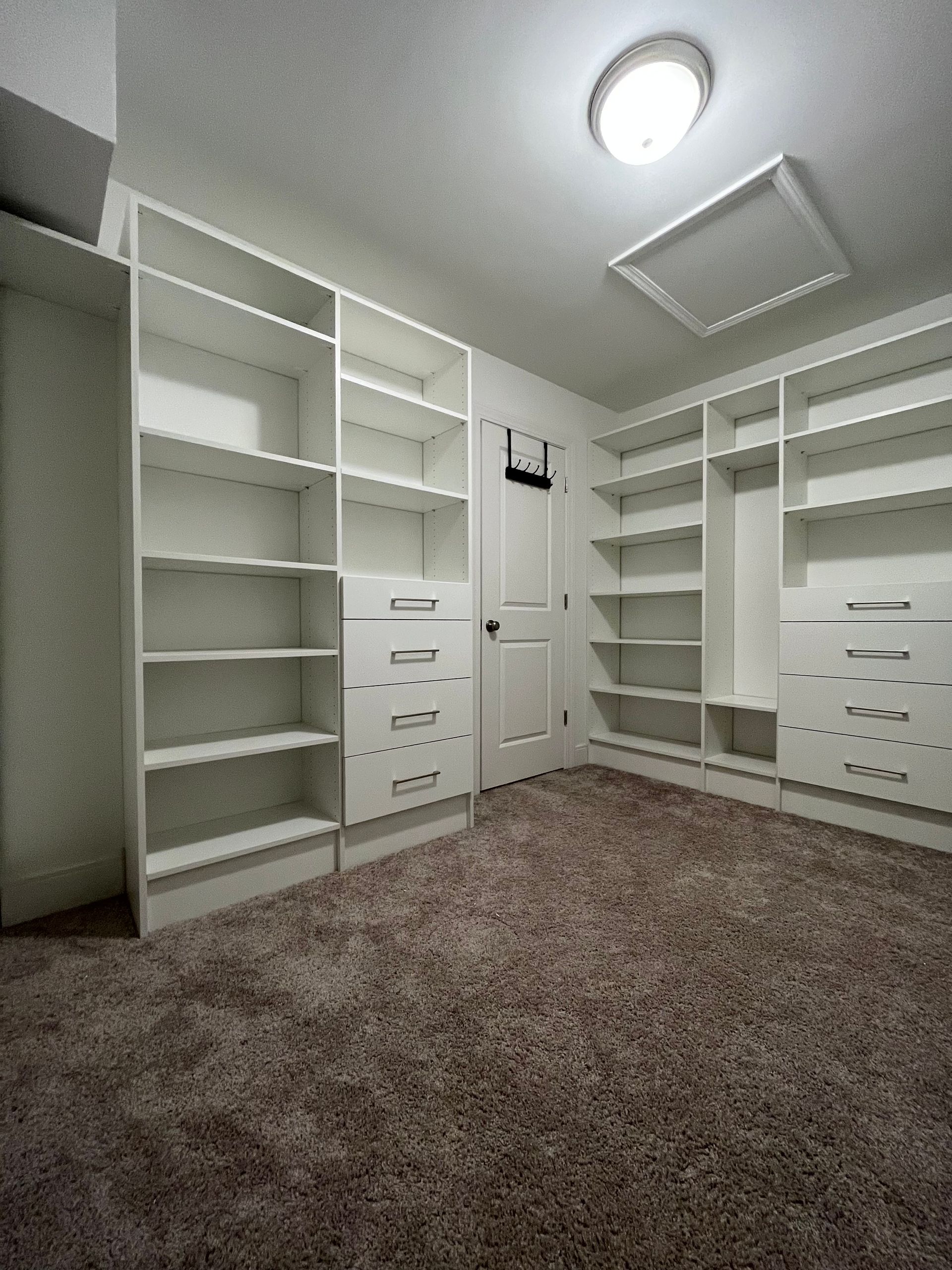 White walk-in closet with shelves and drawers, brown carpet, and a door.