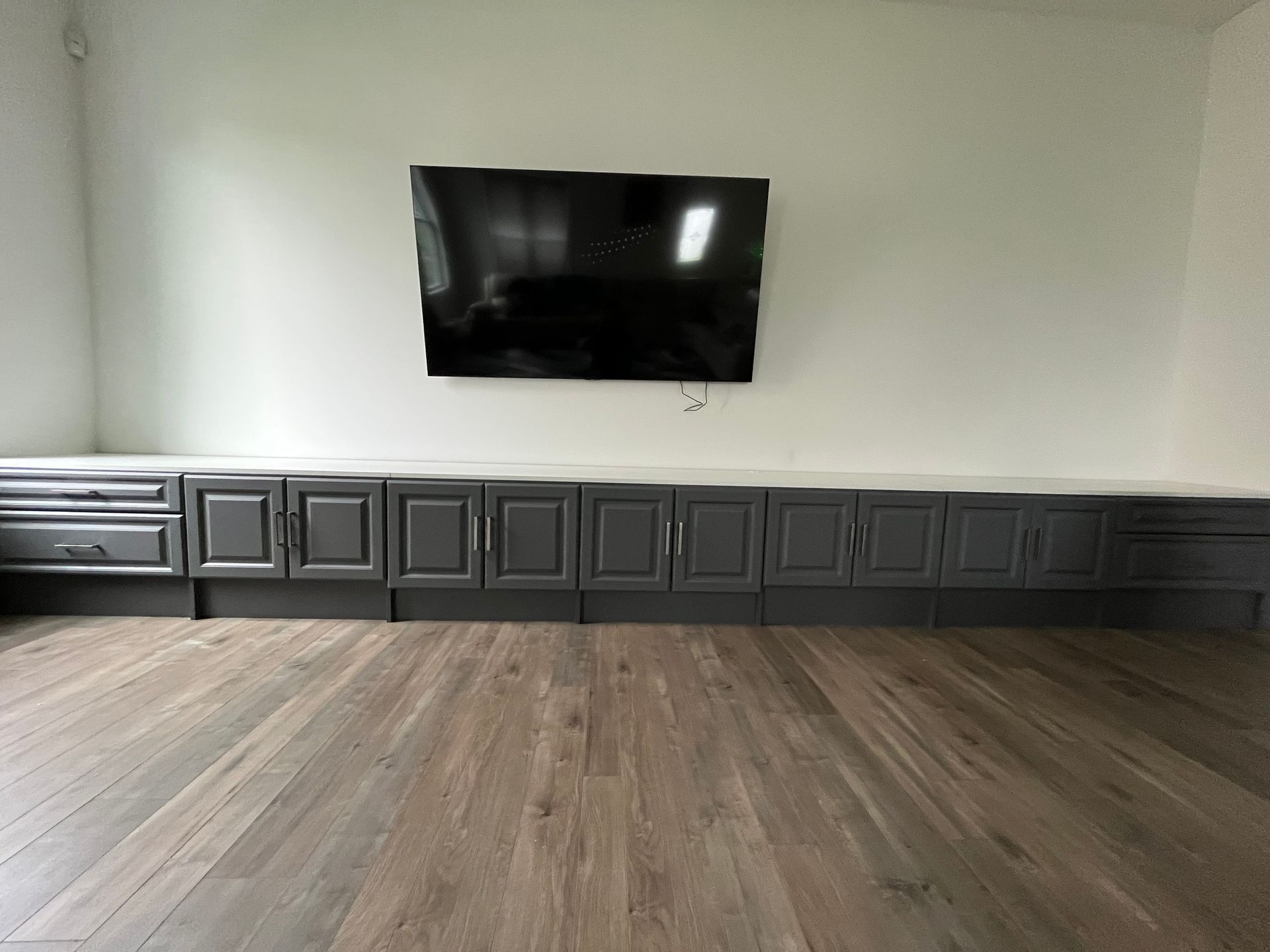 A dark gray entertainment center below a mounted TV on a white wall, with hardwood flooring.