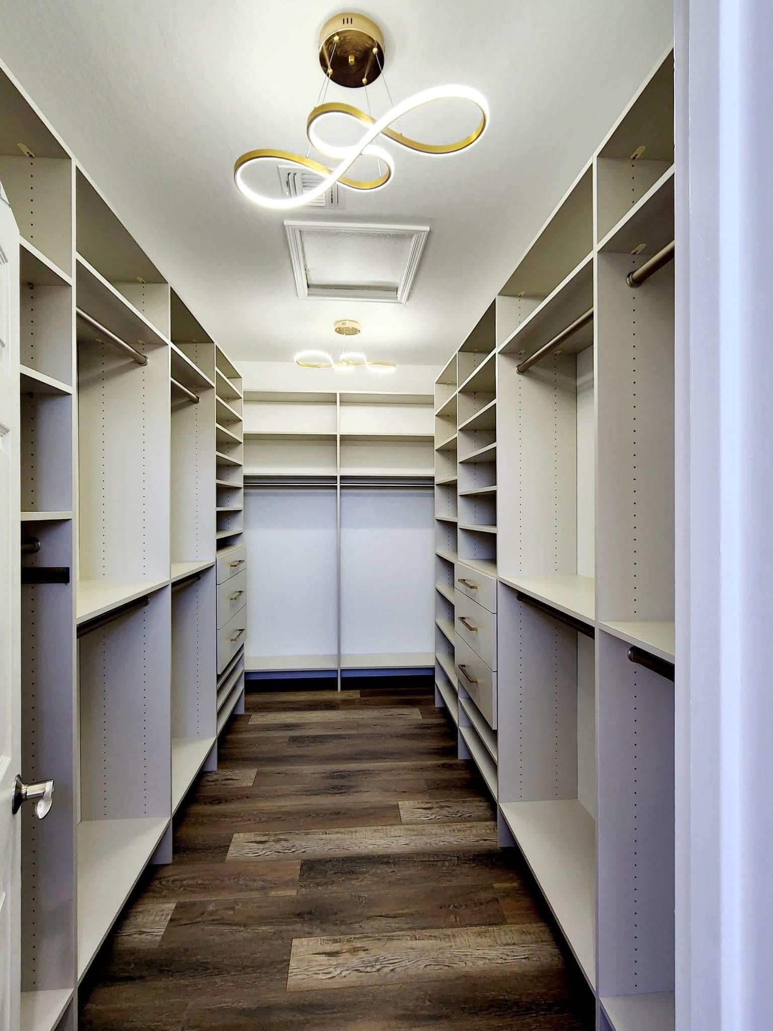 Walk-in closet with white shelves, wooden floor, and modern light fixtures.