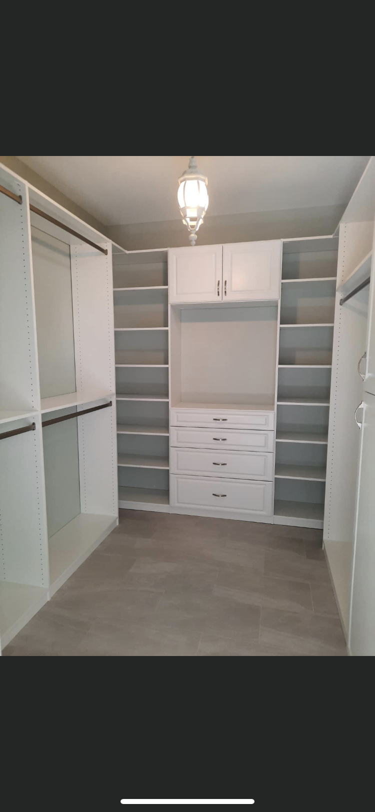 White walk-in closet with built-in shelves, drawers, and hanging rods. Neutral carpet, overhead light.