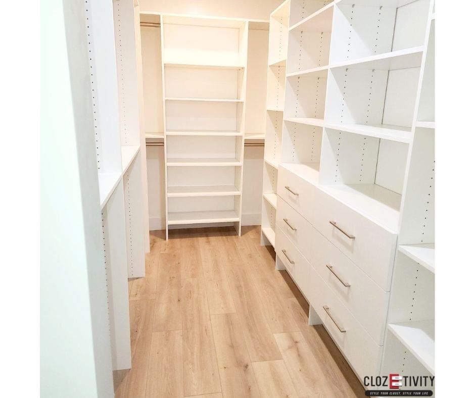 White walk-in closet with shelves, drawers, and wooden flooring. Empty.