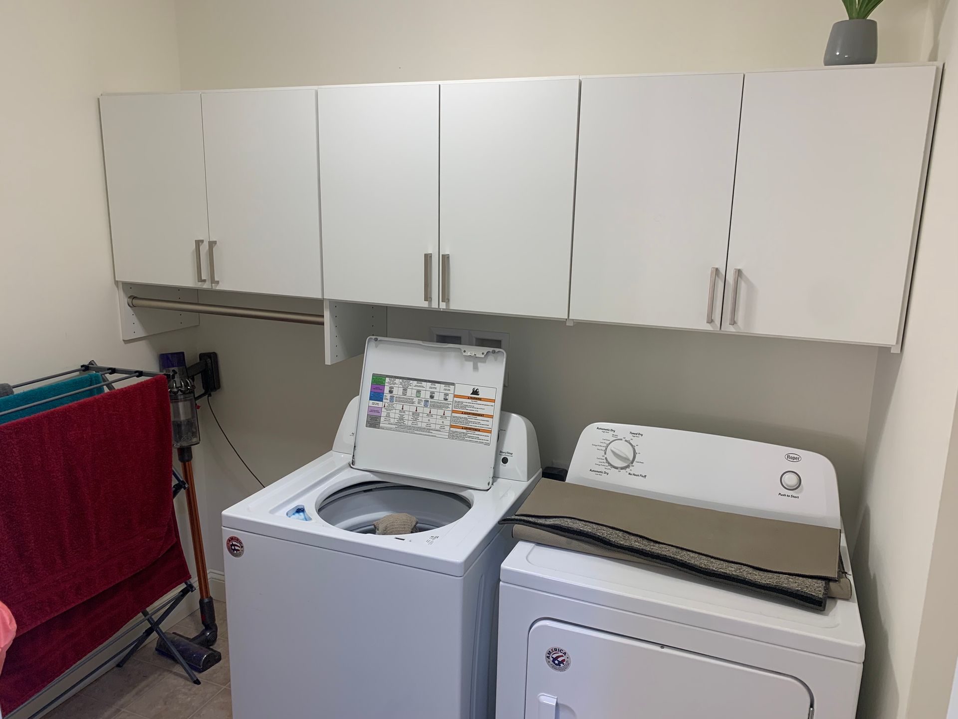Laundry room with white cabinets, washer, dryer, and red ironing board.