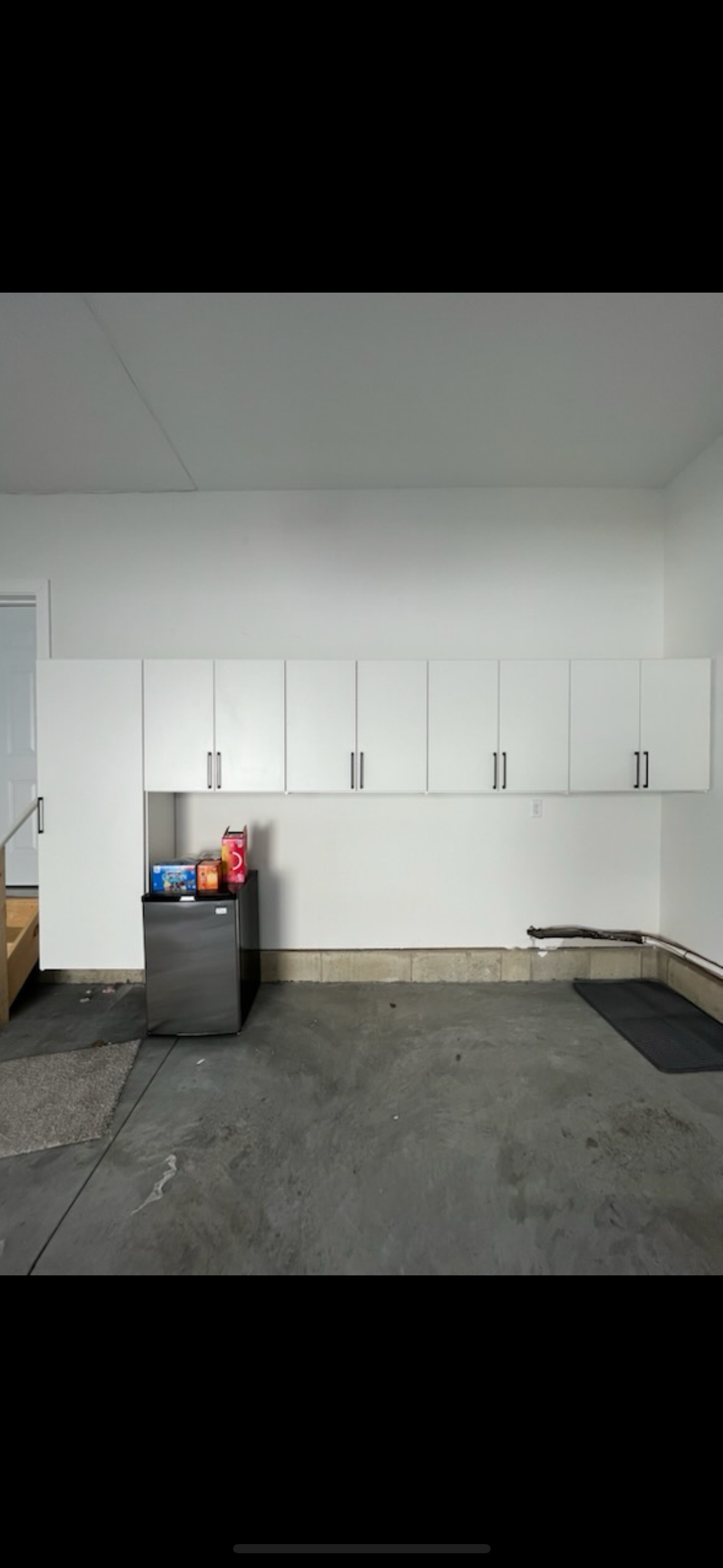Garage with white cabinets, small refrigerator, and a dirty concrete floor.