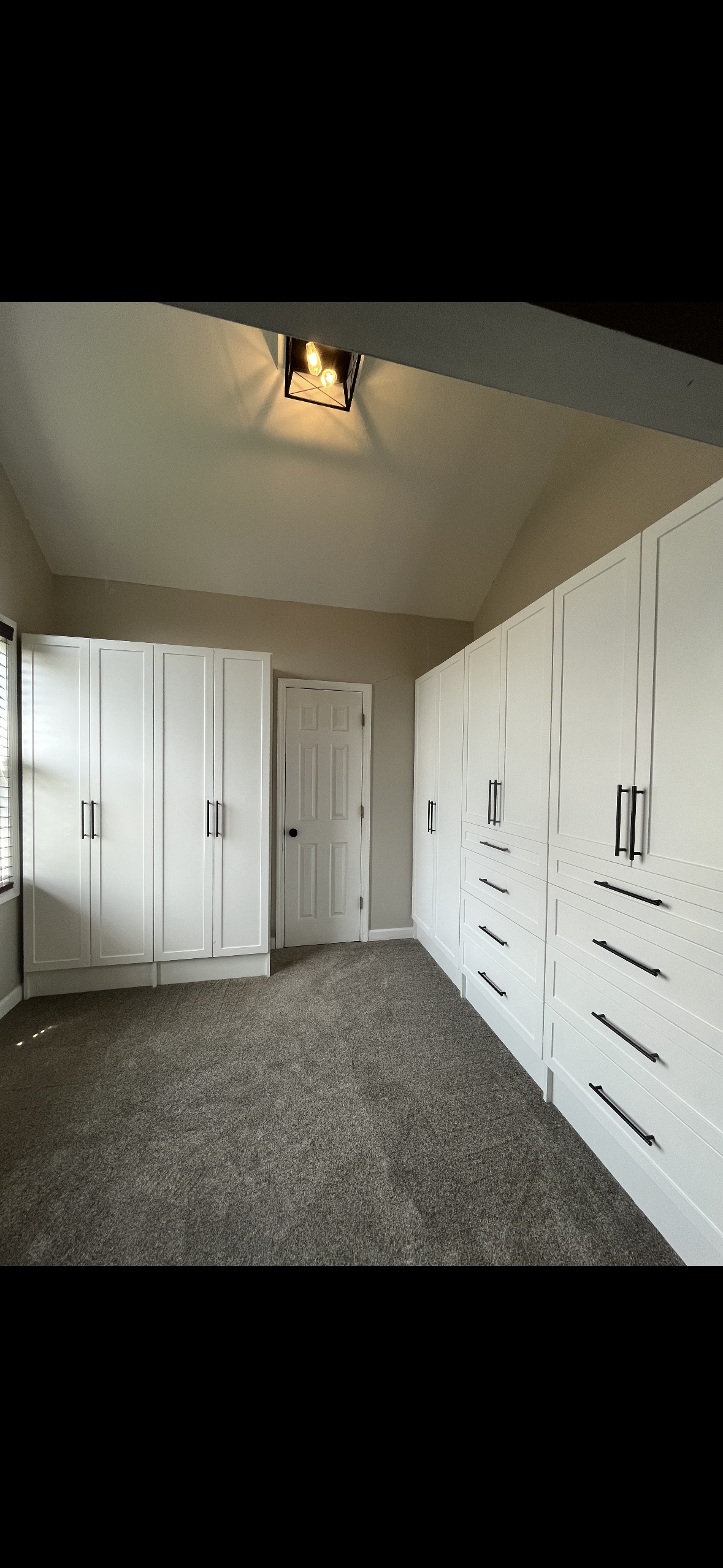 A room with white built-in cabinets and a door, with a textured gray carpet.