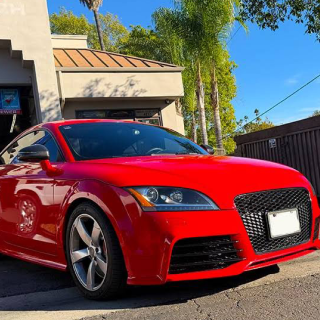 A bright red Audi TT coupe parked on a paved driveway in front of a building with palm trees in the background | Euro Auto Tech & Smog