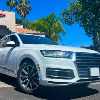 A white Audi Q7 SUV parked in front of a building under a bright blue sky with palm trees | Euro Auto Tech & Smog