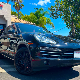 A black Porsche Cayenne SUV parked in a sunny outdoor setting with palm trees and a building in the background | Euro Auto Tech & Smog