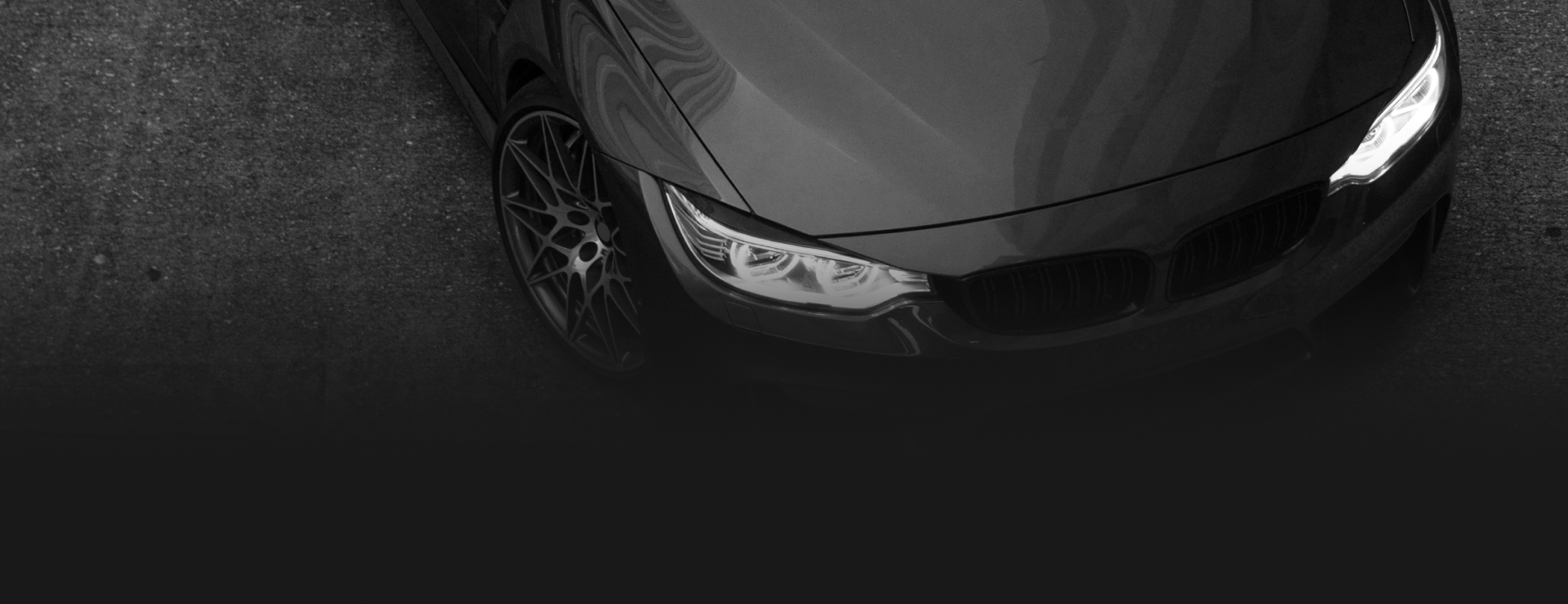 A high-angle view of the front section of a dark-colored BMW car parked on an asphalt surface.