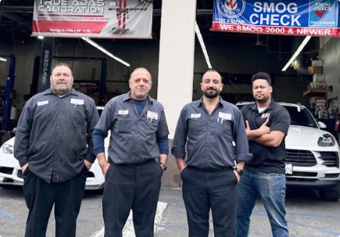 Four staff members in uniform stand in a row outside a service center under Smog Check and Calibration signs | Euro Auto Tech & Smog