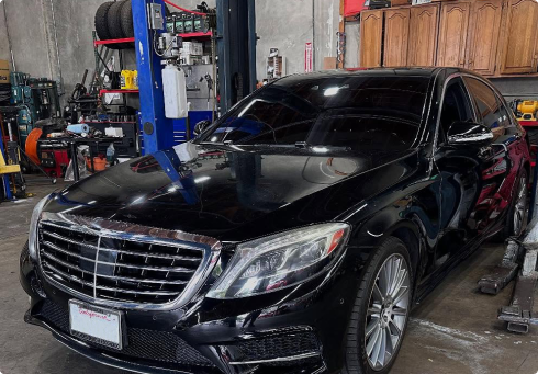 A black Mercedes-Benz sedan parked inside an automotive repair shop with tools and equipment in the background | Euro Auto Tech & Smog