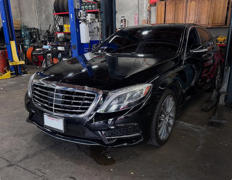 A black Mercedes-Benz S-Class sedan parked inside an automotive repair shop with garage equipment in the background | Euro Auto Tech & Smog